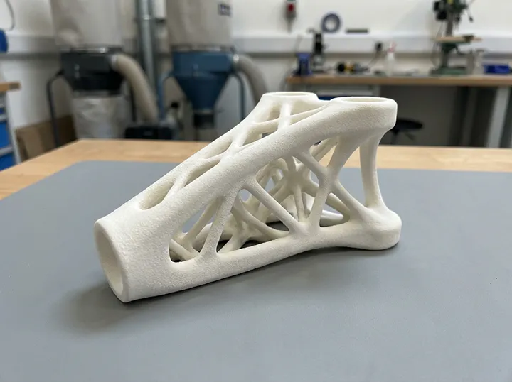 sls-printing-white-sintered-nylon-lattice-part SLS teknolojisiyle sinterlenmiş, karmaşık kafes (lattice) geometrilere sahip beyaz renkli dayanıklı prototip.