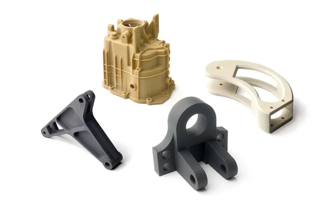 Beyaz zemin üzerinde, ULTEM, Naylon ve Karbon Fiber gibi farklı FDM malzemeleriyle üretilmiş karmaşık geometrili endüstriyel yedek parçalar ve prototipler.